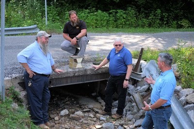 Pictured above: IACMI Technology Impact Manager John Unser, second from right, is coordinating a public-private collaboration to install a fiber reinforced polymer composite bridge deck in a rural Tennessee community. From left, are Morgan County (TN) Highway Superintendent Joe Henry Miller, McKinney Excavating (TN) Owner Brian McKinney, and Composite Applications Group CEO Jeff McCay.